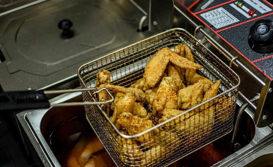 Een professionele horeca friteuse in een drukke keuken met gefrituurde snacks en een chef-kok die aan het werk is.
